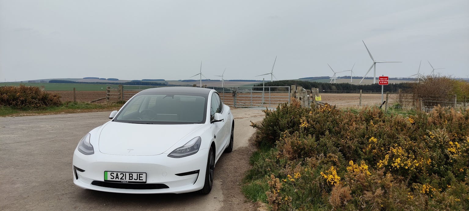 Image shows a Tesla next to a wind farm 